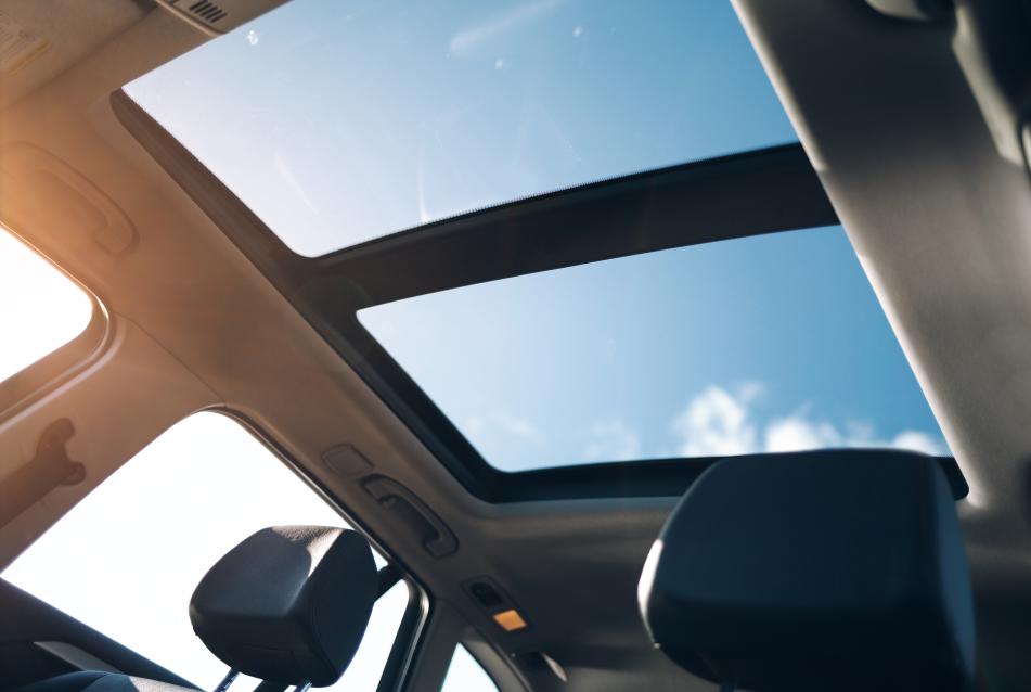 A black automotive panoramic roof illuminated by sunlight.